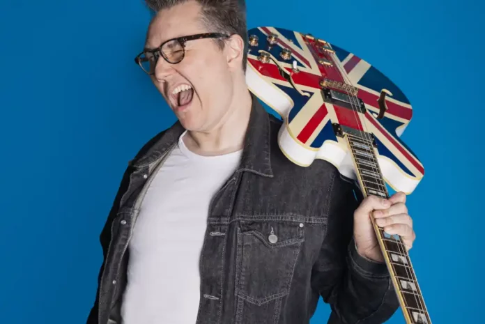 britpopshow Comedian Marc Burrows with guitar against blue background