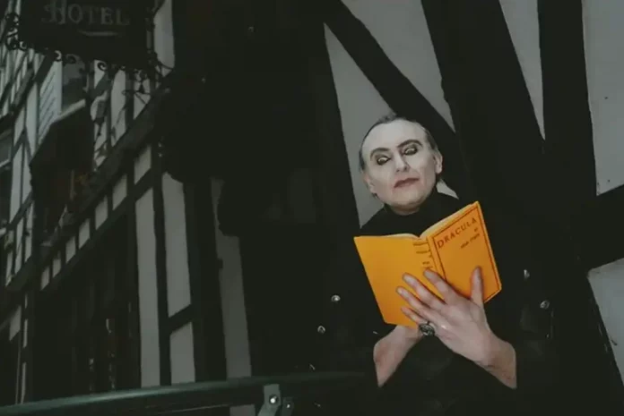 Person dressed as Dracula reading a yellow book outdoors.